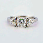 Trendig platinaring med tre gnistrande moissaniter – cushion‑cut mittsten, två trillionslipade sidostenar, och infattning i rödguld