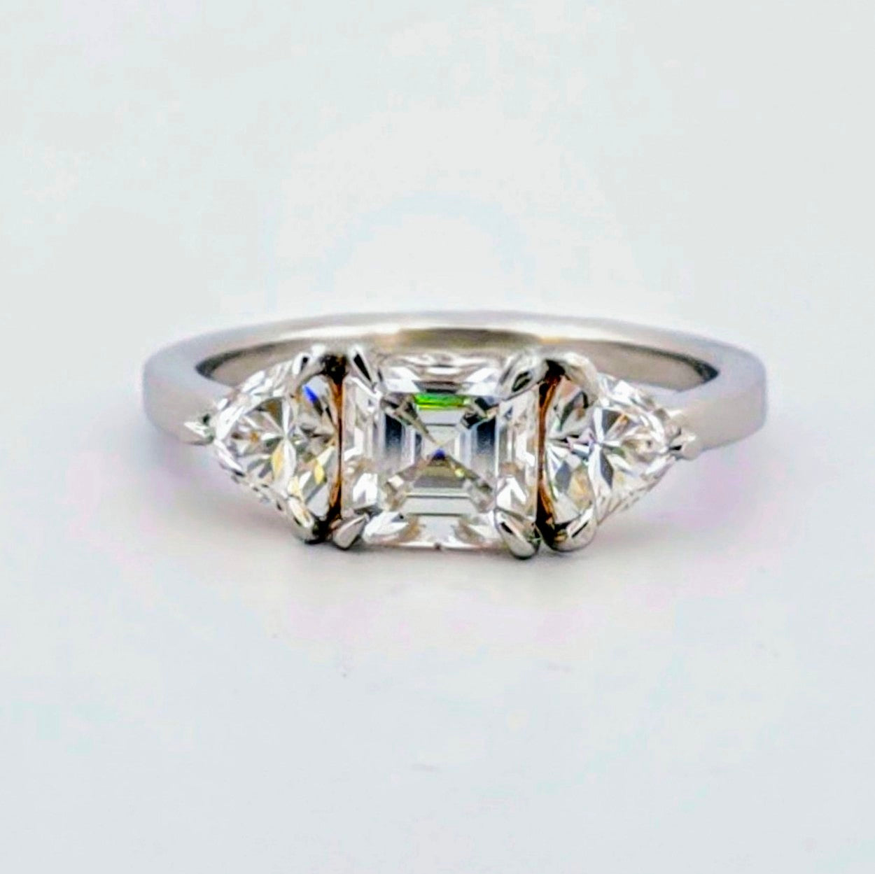 Trendig platinaring med tre gnistrande moissaniter – cushion‑cut mittsten, två trillionslipade sidostenar, och infattning i rödguld