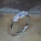 Trendig platinaring med tre gnistrande moissaniter – cushion‑cut mittsten, två trillionslipade sidostenar, och infattning i rödguld