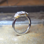 Trendig platinaring med tre gnistrande moissaniter – cushion‑cut mittsten, två trillionslipade sidostenar, och infattning i rödguld