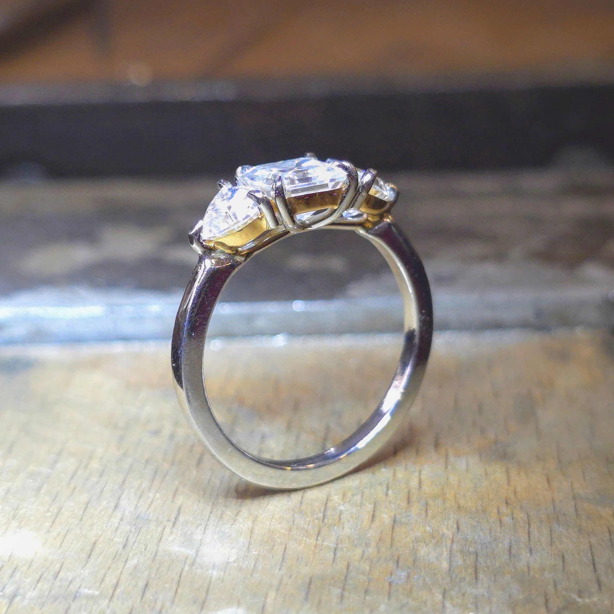 Trendig platinaring med tre gnistrande moissaniter – cushion‑cut mittsten, två trillionslipade sidostenar, och infattning i rödguld