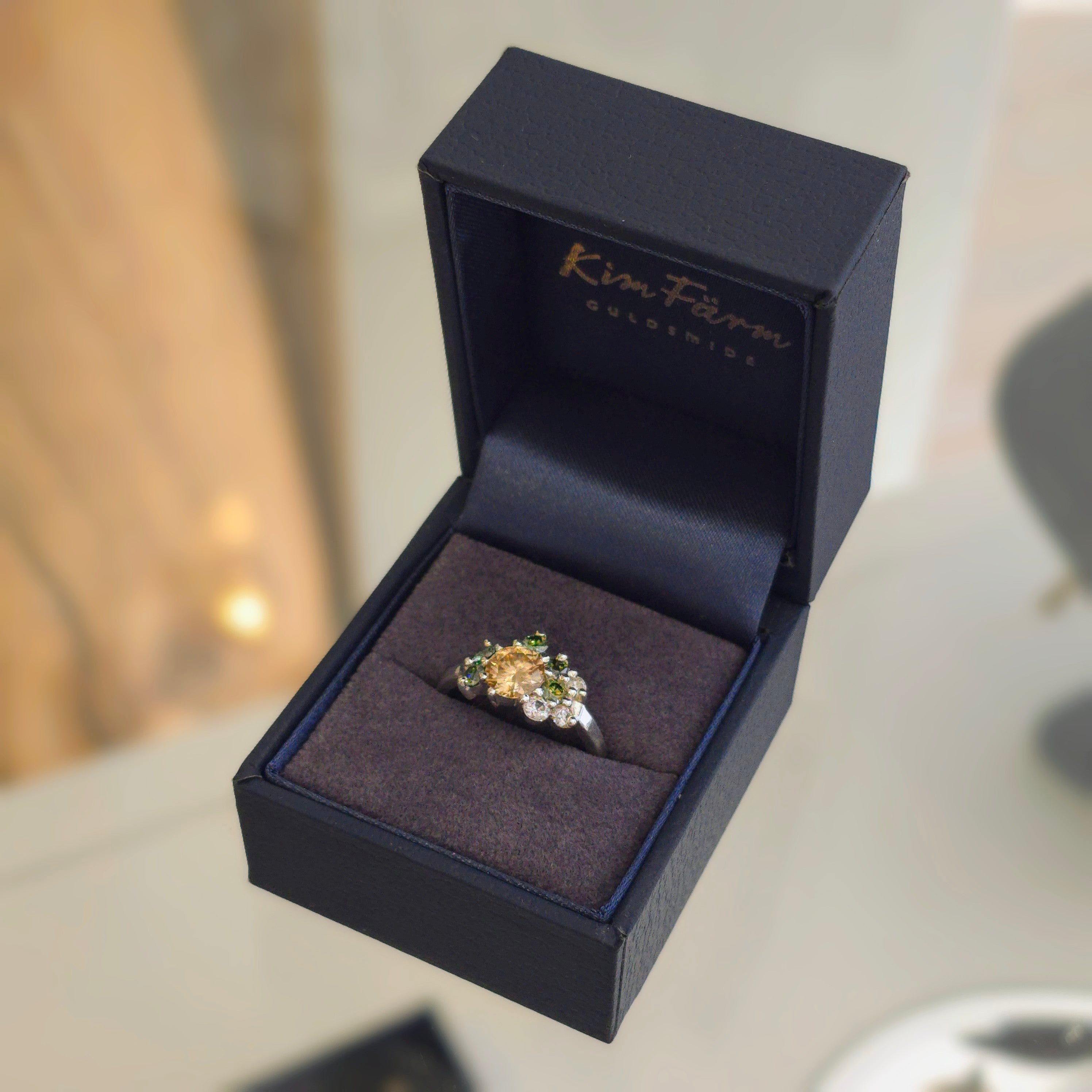 Silverring med orange och gröna moissaniter i elegant handgjord design mot neutral bakgrund.