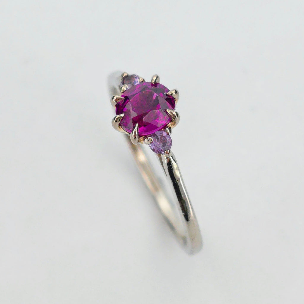 Platina ring med infattning i 18K rödguld, med granat och alexandriter, handgjord lyxdesign mot vit bakgrund.