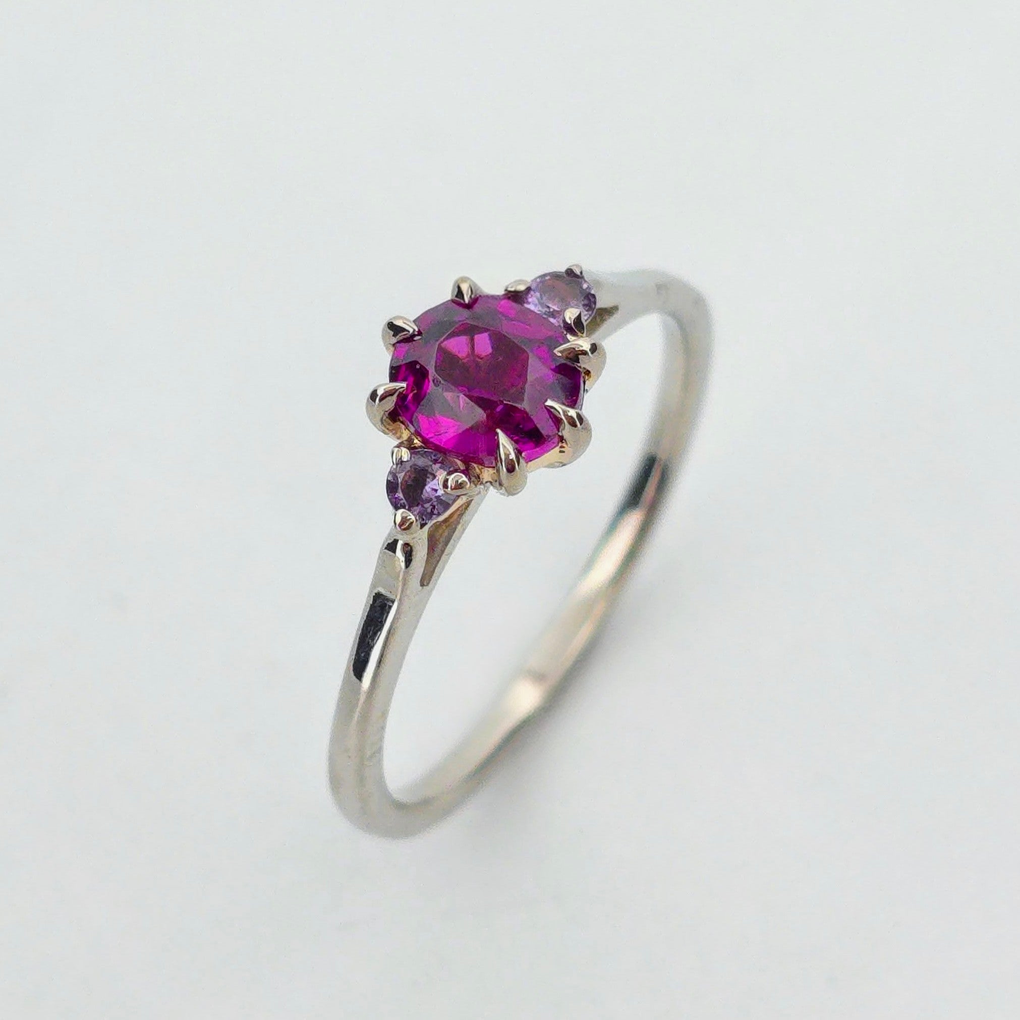 Platina ring med infattning i 18K rödguld, med granat och alexandriter, handgjord lyxdesign mot vit bakgrund.