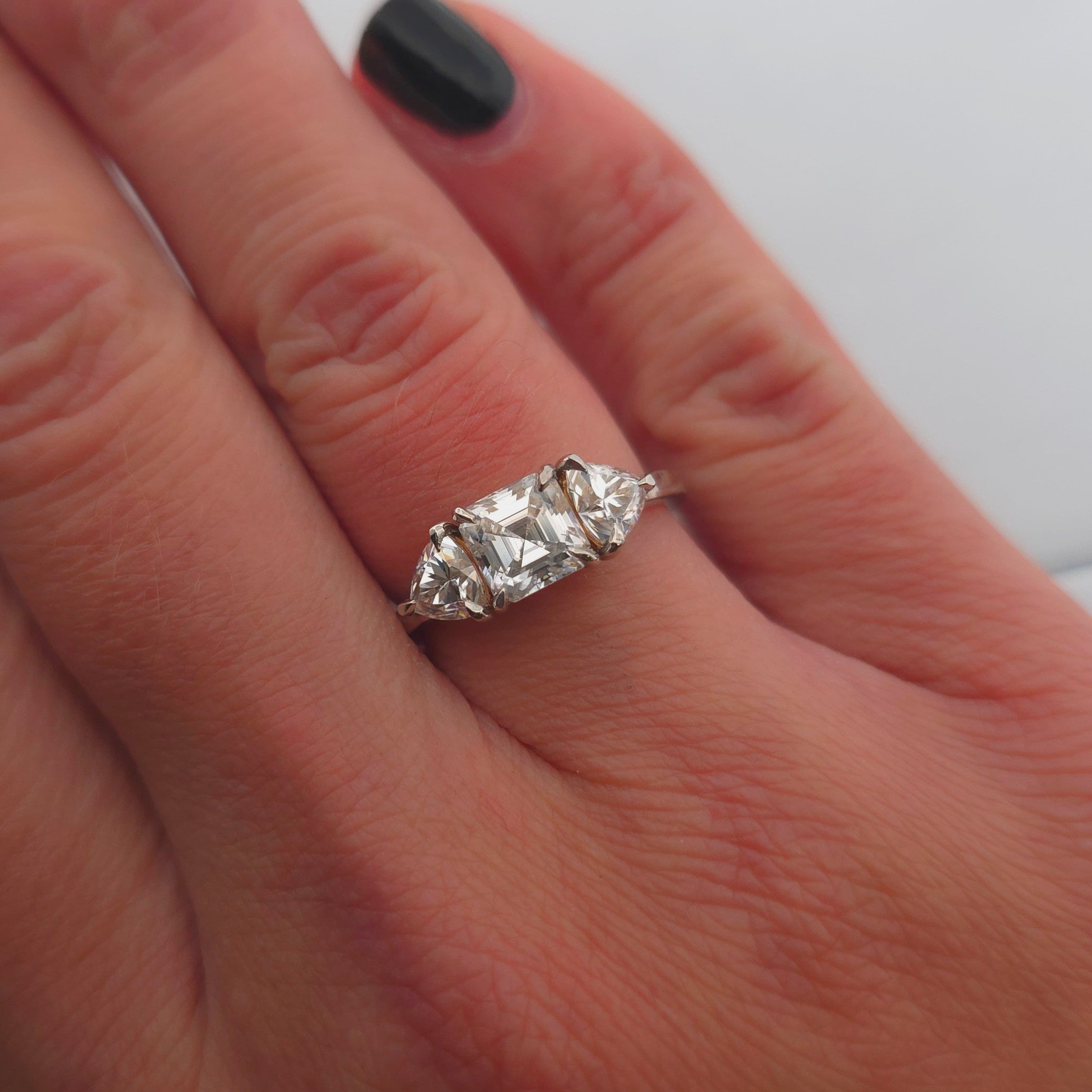 Trendig platinaring med tre gnistrande moissaniter – cushion‑cut mittsten, två trillionslipade sidostenar, och infattning i rödguld