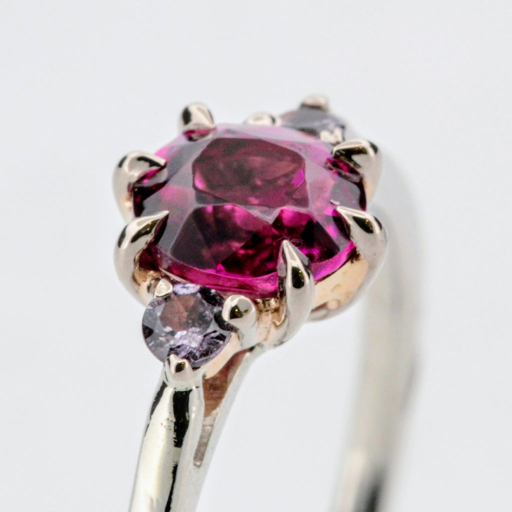 Platina ring med infattning i 18K rödguld, med granat och alexandriter, handgjord lyxdesign mot vit bakgrund.