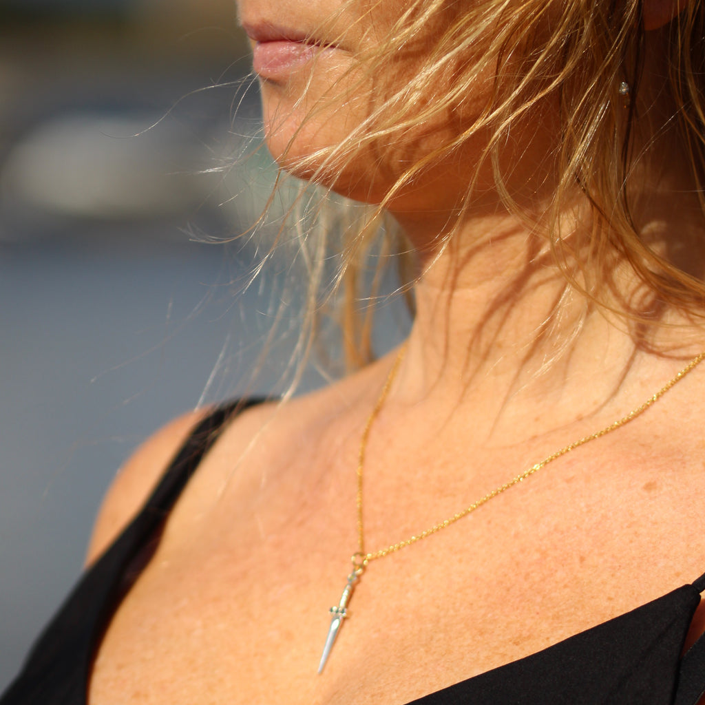 Ett hängsmycke formad som en liten silversvärd med en guldkedja. Svärdets fäste är prytt med svarta ädelstenar, och en ljus sten sitter högst upp på handtaget.