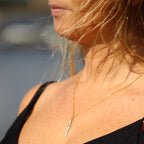 Ett hängsmycke formad som en liten silversvärd med en guldkedja. Svärdets fäste är prytt med svarta ädelstenar, och en ljus sten sitter högst upp på handtaget.